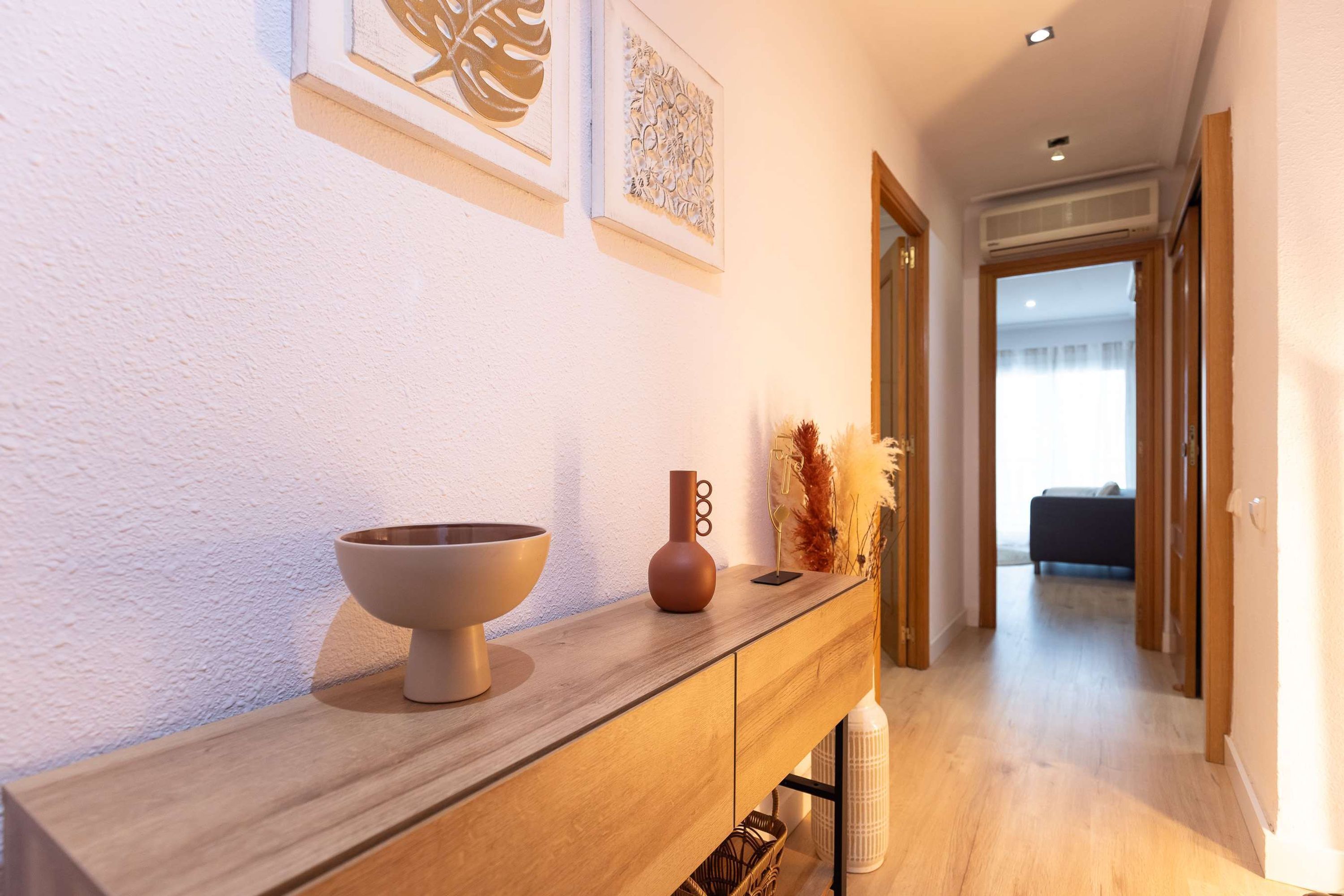 Un pasillo con una consola de madera, un cuenco, un florero y decoración en la pared.