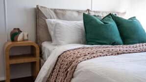 Una cama bien hecha con un plaid tejido, una mesita de noche de madera con un jarrón de cerámica y una almohada verde.