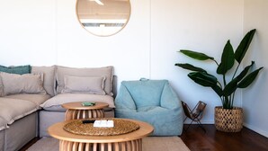 Una sala de estar acogedora con un sofá modular, una mesa de centro redonda de madera, un sillón azul, una planta grande en maceta y una cesta tejida.