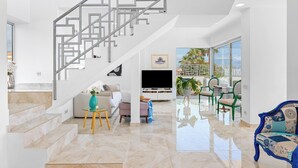 Un vaste espace de vie agrémenté d’un escalier moderne, d’un téléviseur à écran plat et d’un coin salon offrant une vue sur l’extérieur.