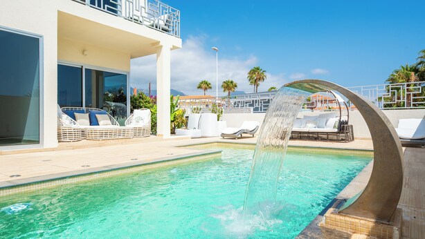 Une piscine agrémentée d’un élément décoratif aquatique, de chaises longues et offrant une vue sur le paysage environnant.
