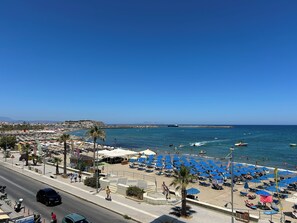 Ein Strand mit blauen Sonnenschirmen, einer Promenade und Blick aufs Meer.
