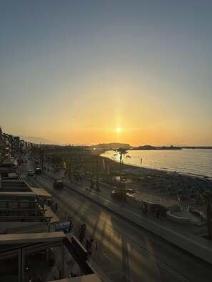 Eine Küstenstadtlandschaft im Sonnenuntergang mit einer Straße, die zu einem Strand führt, Palmen und einem klaren Himmel.