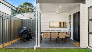A patio with a table and chairs, a barbecue grill, and a ceiling fan.