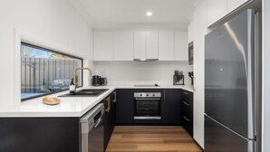 A modern kitchen with white cabinets, a black countertop, stainless steel appliances, and a wooden floor.