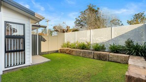 A residential backyard with a house, a white fence, and a well-maintained lawn.