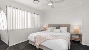 A bedroom with a bed, two bedside tables, a ceiling fan, and a window with blinds.
