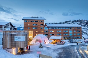 A modern hotel with multiple floors, a ski resort in the background, and a snow-covered landscape.