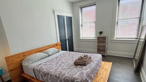 Una camera da letto con un letto, una cassettiera e due finestre con tende.