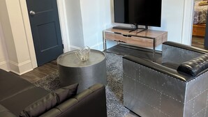 Un soggiorno moderno con un divano nero, un tavolino in vetro, un televisore a schermo piatto su un supporto in legno e un quadro astratto grigio sulla parete.