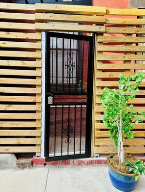 Una cerca de madera con un portón negro, una planta en maceta y una base de concreto.