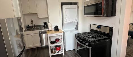 A compact kitchen with a refrigerator, stove, microwave, and a small island with pots.