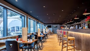 Ein modernes Restaurant mit Holzböden, schwarzen Stühlen und einer Bar mit Hockern.