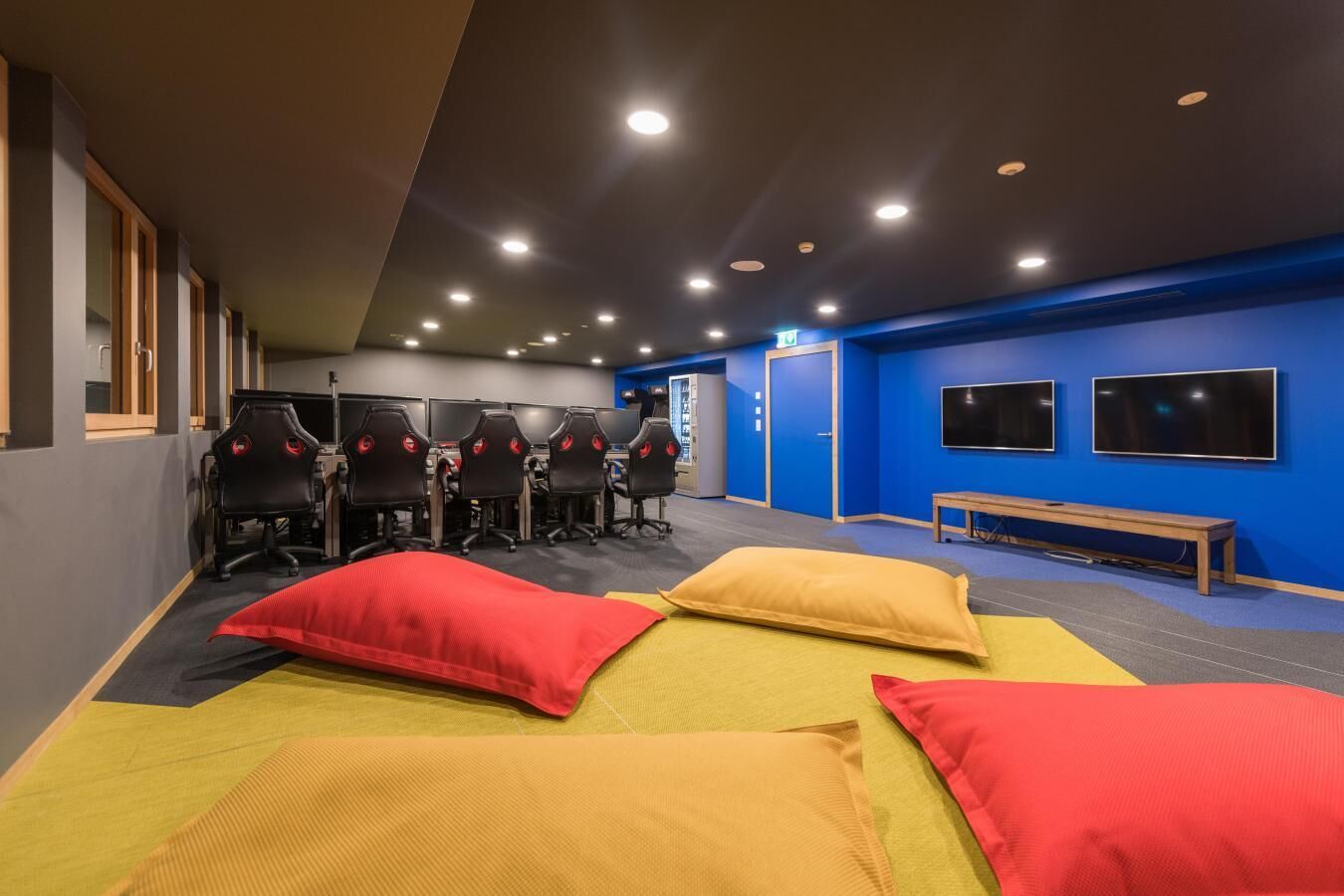A modern gaming lounge with multiple gaming stations, a bench, and a blue accent wall.