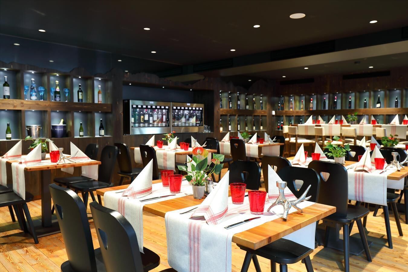 A restaurant with multiple tables set for dining, each with a white tablecloth, red napkins, and red glasses.