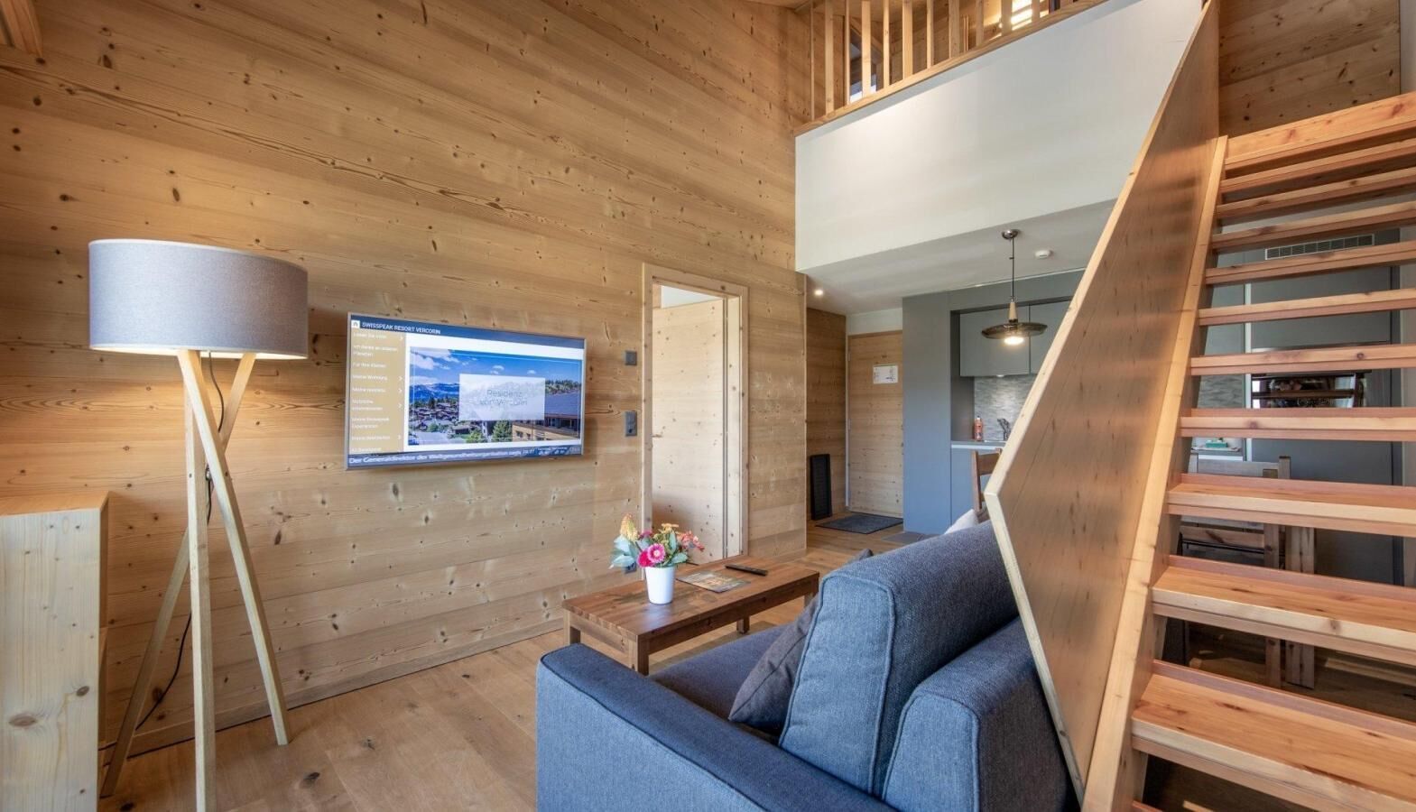 A modern interior with wooden walls, a sofa, a lamp, and a TV displaying a resort.