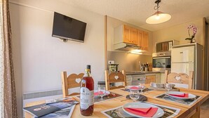 A dining area with a table set for four, a bottle of wine, and a television mounted on the wall.