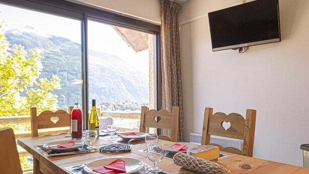 A dining table set with plates, glasses, and a bottle, with a mountain view through large windows.
