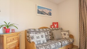 A cozy room with a patterned sofa, a wooden side table with a potted plant, a framed picture on the wall, and a curtain.