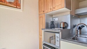 A compact kitchen with wooden cabinets, a stainless steel sink, a kettle, and an oven. - 10m from ski slopes, Ground floor, terrace, 27m², Aussois (Aussois)