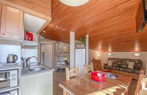 Kompakti keittiö moderneilla laitteilla, ruokailutila puupöydällä sekä viihtyisä oleskelualue, jossa on sohva.