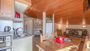 A compact kitchen with wooden ceiling, a dining area with a table and chairs, and a sofa in the living area. - 150m from resort center, Ground floor, terrace, 27m², Aussois (Aussois)
