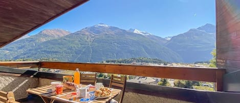 A wooden table with chairs on a balcony overlooking a mountainous landscape.