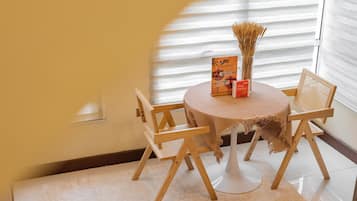 Una mesa redonda pequeña con mantel tejido, dos sillas de madera, un atril para menús y un florero con plantas secas.