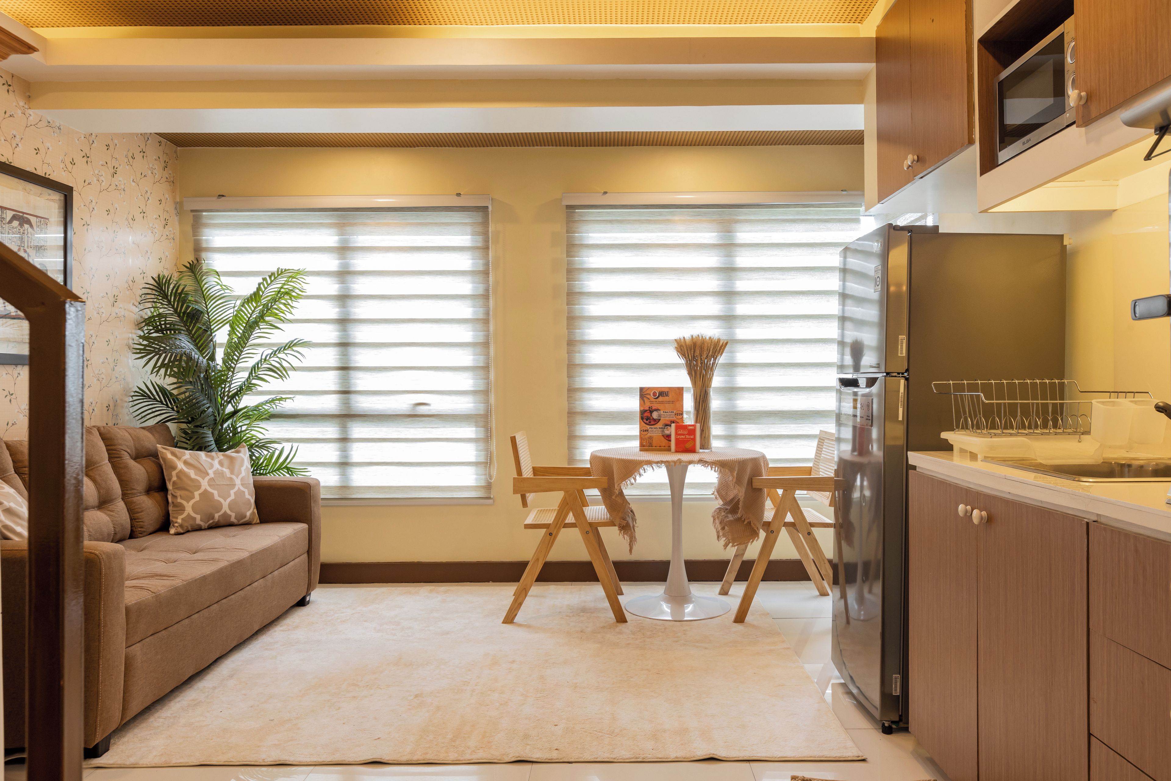 Una sala de estar con sofá, una mesa de comedor con sillas, una planta en maceta y una cocina con microondas y refrigerador.