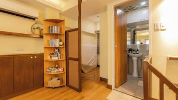 A hallway with a wooden floor, a bookshelf with various items, a door leading to a bathroom, and a small rug.