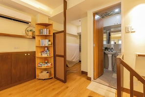 A hallway with a wooden floor, a bookshelf with various items, a door leading to a bathroom, and a small rug. -     The BGC Loft Modern 1BR City Stay in Fort Victoria, BGC (Taguig)