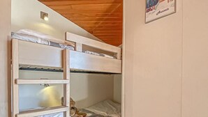 Une chambre avec des lits superposés, un plafond en bois et un tableau encadré au mur.