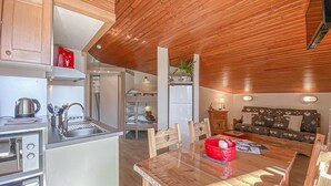 Une cuisine compacte avec un plafond en bois, un coin repas avec une table et des chaises, et un canapé dans l’espace salon.