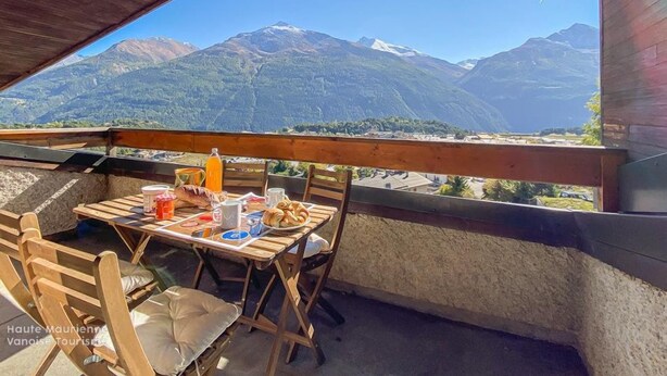 Mesa de madera con sillas en un balcón con vistas a un paisaje montañoso.