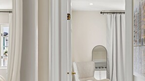 A hallway with a white chair, a mirror, and a fluffy rug.