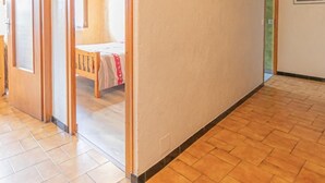A hallway with a wooden floor, a door leading to a room with a bed, and a wall-mounted light fixture.