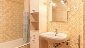 A bathroom with patterned wallpaper, a white sink, a mirror, a shower curtain, and a towel rack.