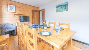 A wooden dining table set with chairs, a television, and a scenic painting on the wall.