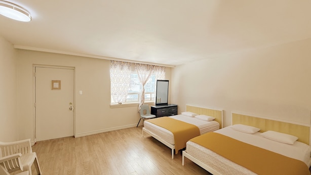 Ein Hotelzimmer mit zwei Betten, einem Schreibtisch, einem Stuhl, einem Fenster mit Vorhängen und einer Tür.