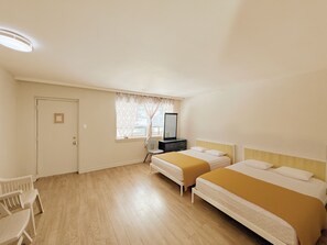 A hotel room with two beds, a desk, a chair, a window with curtains, and a door.