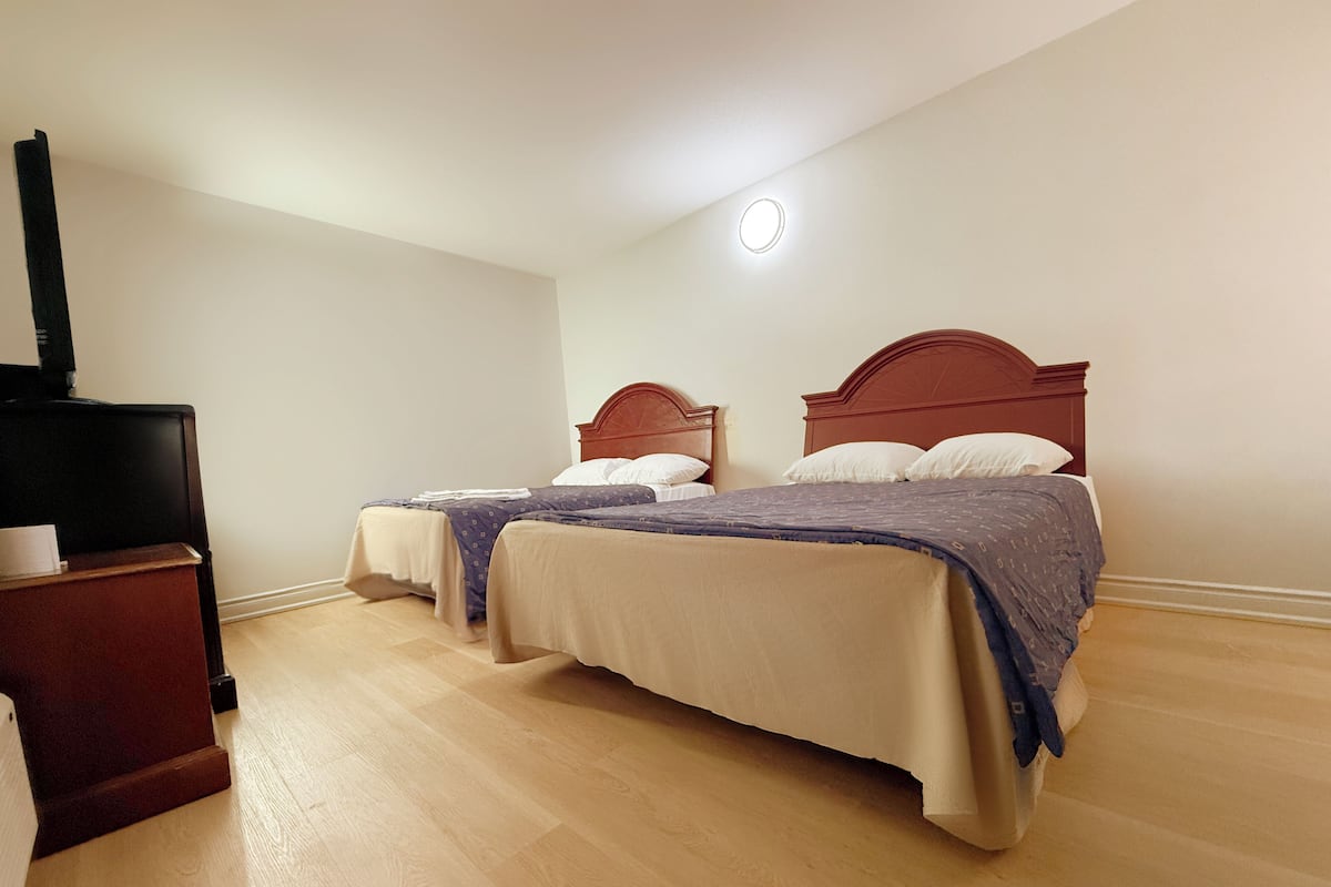 A hotel room with two beds, a TV stand, and a ceiling light.
