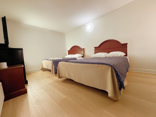 Una habitación de hotel con dos camas, un mueble para televisión y una lámpara en el techo.
