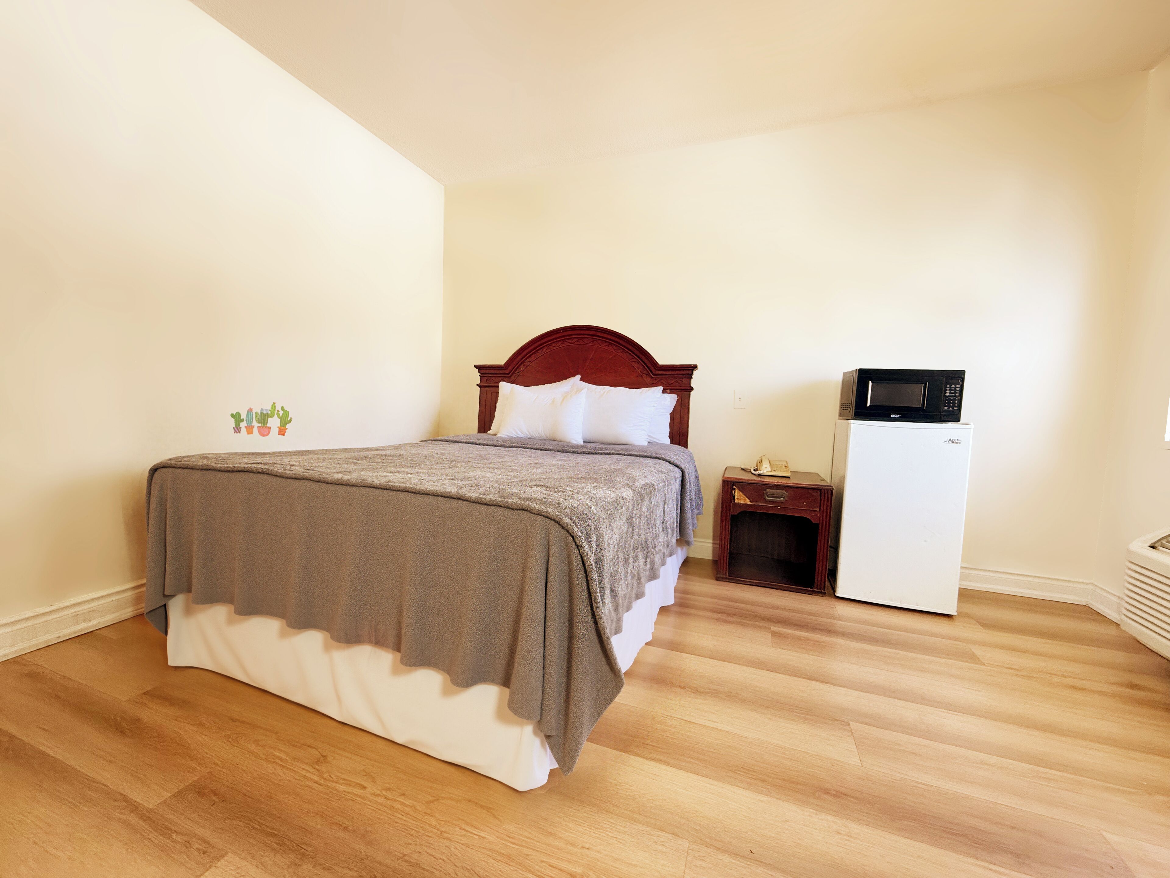 A bedroom with a bed, a nightstand, a microwave, and a refrigerator.