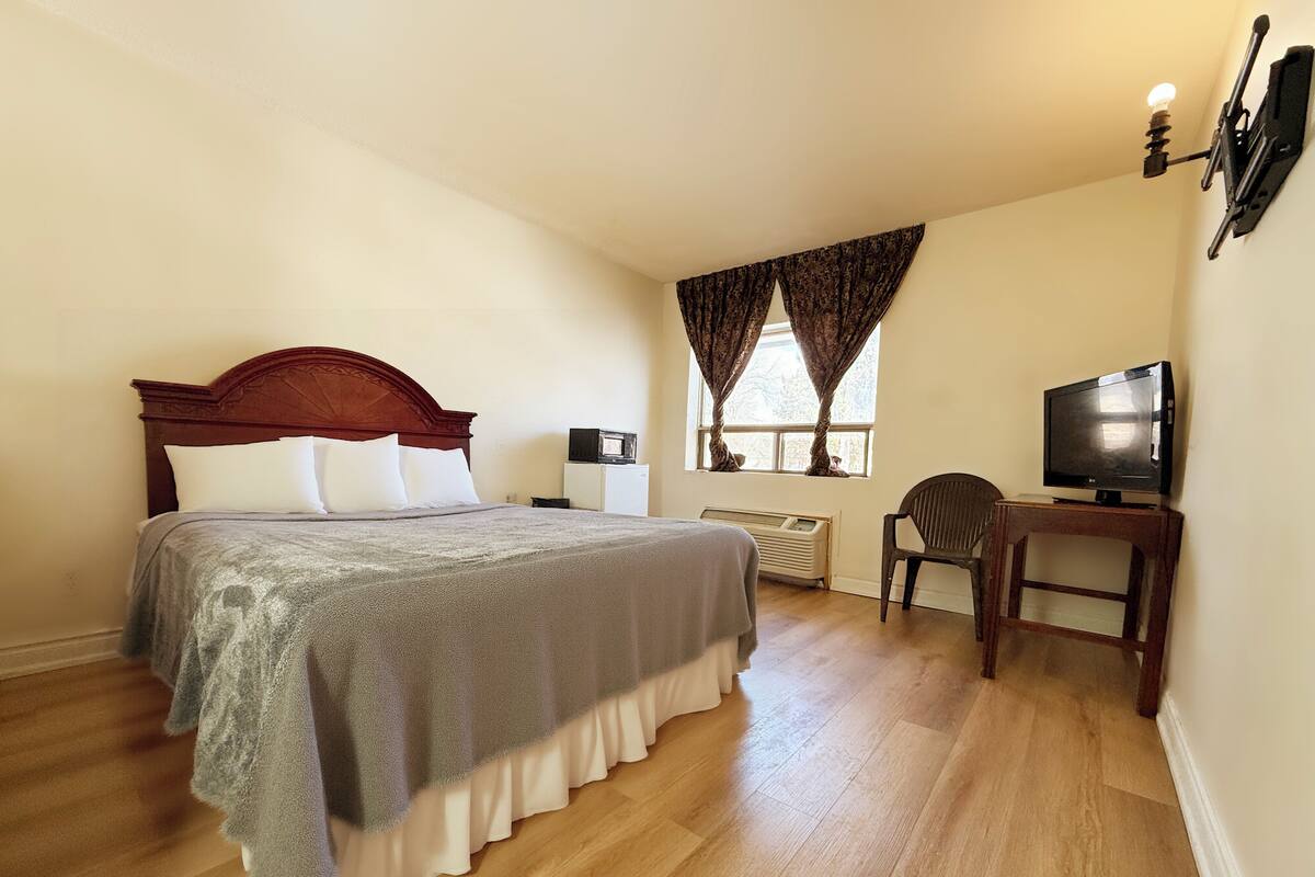 A bedroom with a wooden bed, a desk with a television, a chair, and a window with curtains.