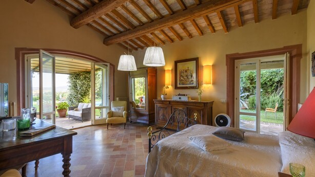 Un dormitorio espacioso con una cama grande, techo de madera y vistas al jardín a través de una puerta abierta.