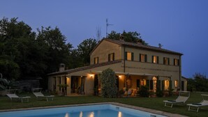 Una casa de dos pisos con piscina, mobiliario exterior y un jardín cuidado.