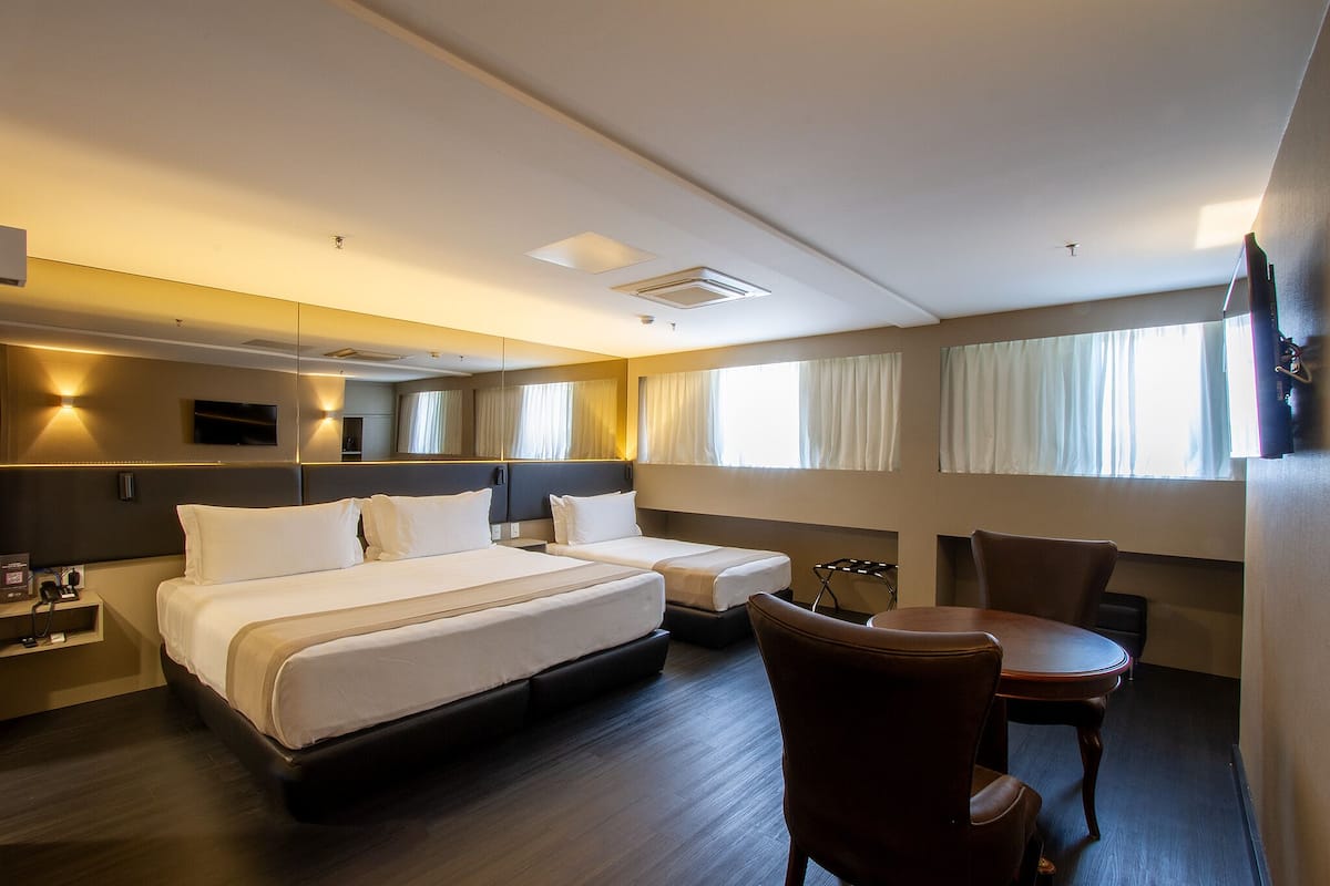 A hotel room with a large bed, a smaller bed, a desk, a chair, a TV, and a window with curtains.