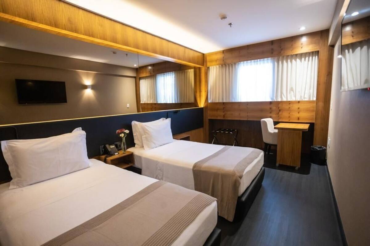 A hotel room with two beds, a desk, a chair, a TV, and a mirror.
