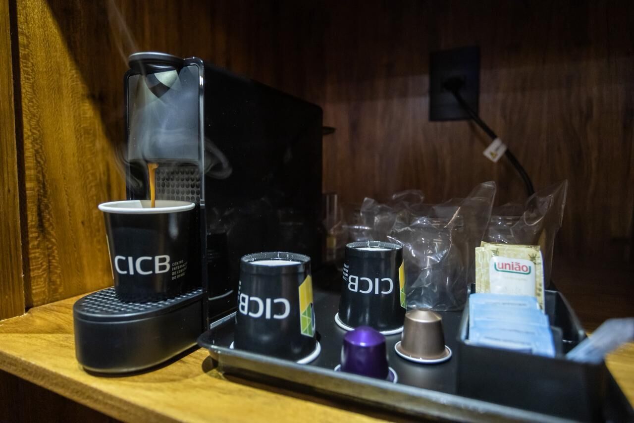 Una máquina de café con tazas desechables etiquetadas 'CICB' y una bandeja con bolsas de plástico y un paquete de té 'união'.