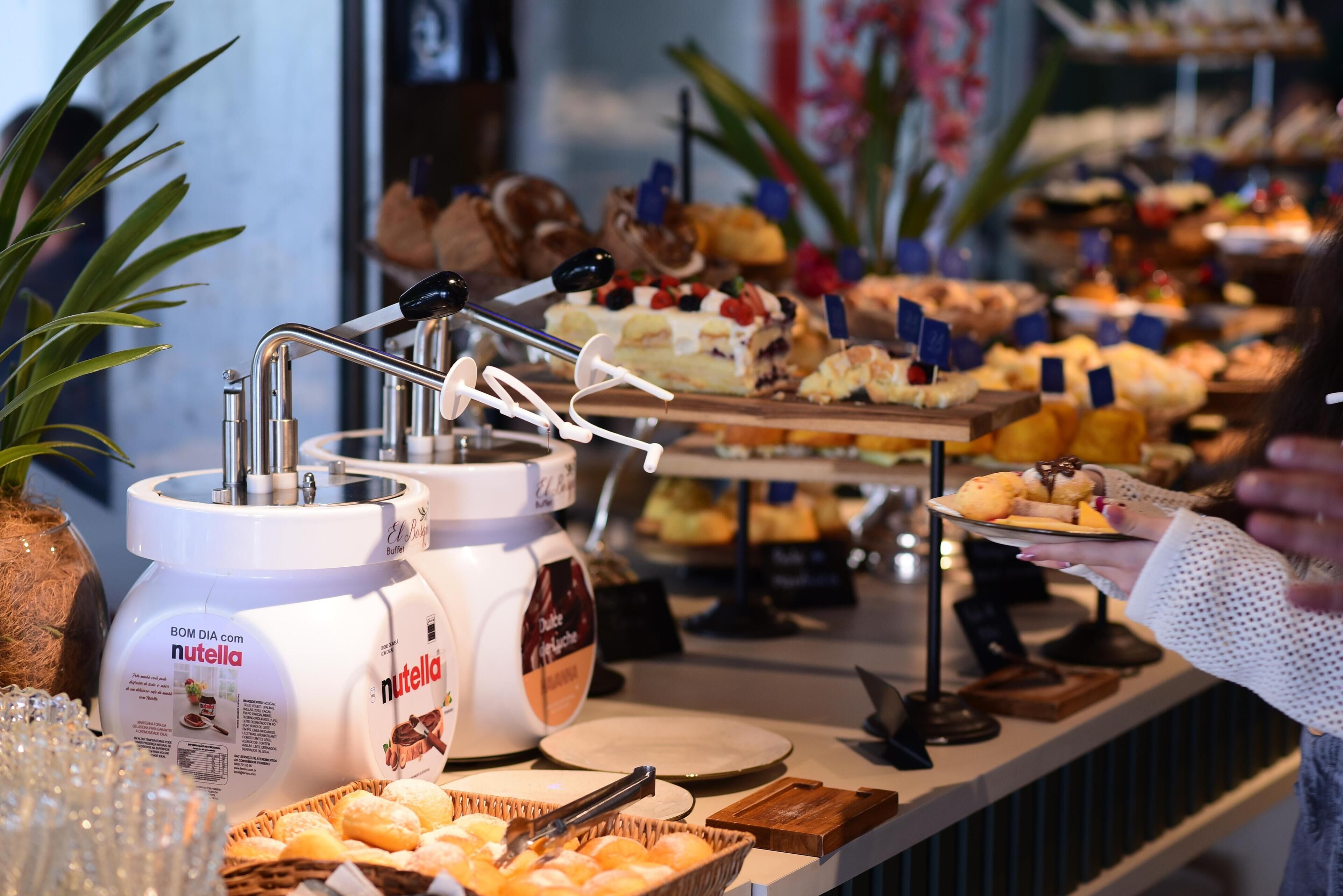 A buffet with various food items and two large containers of Nutella.